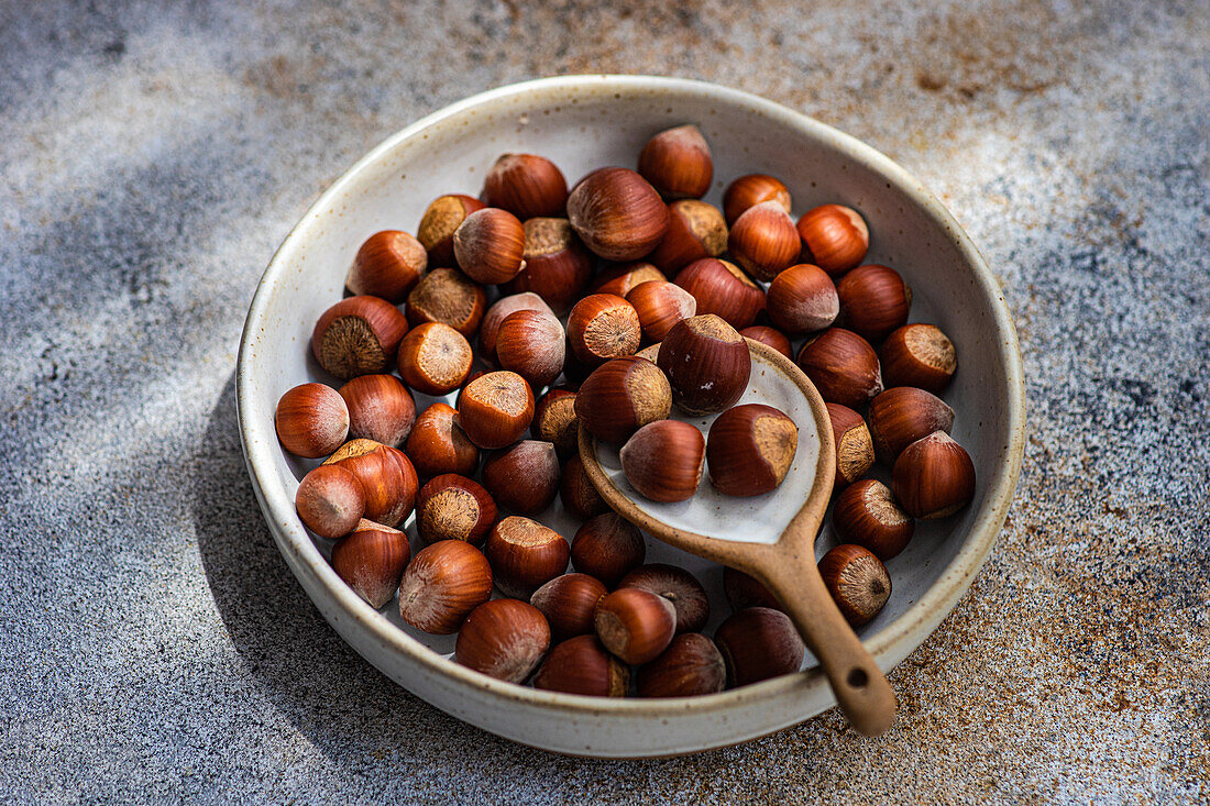 Top view of fresh chestnuts placed in ceramic bowl with a spoon in a concrete background