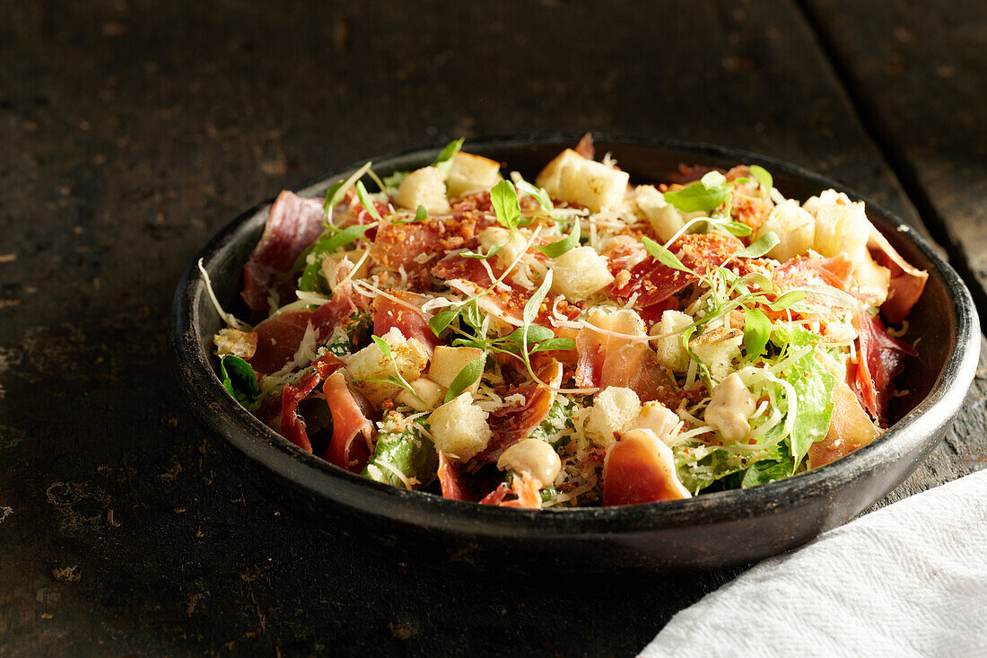 High angle of appetizing salad consisting of fresh chopped vegetables herbs and bacon served in black bowl