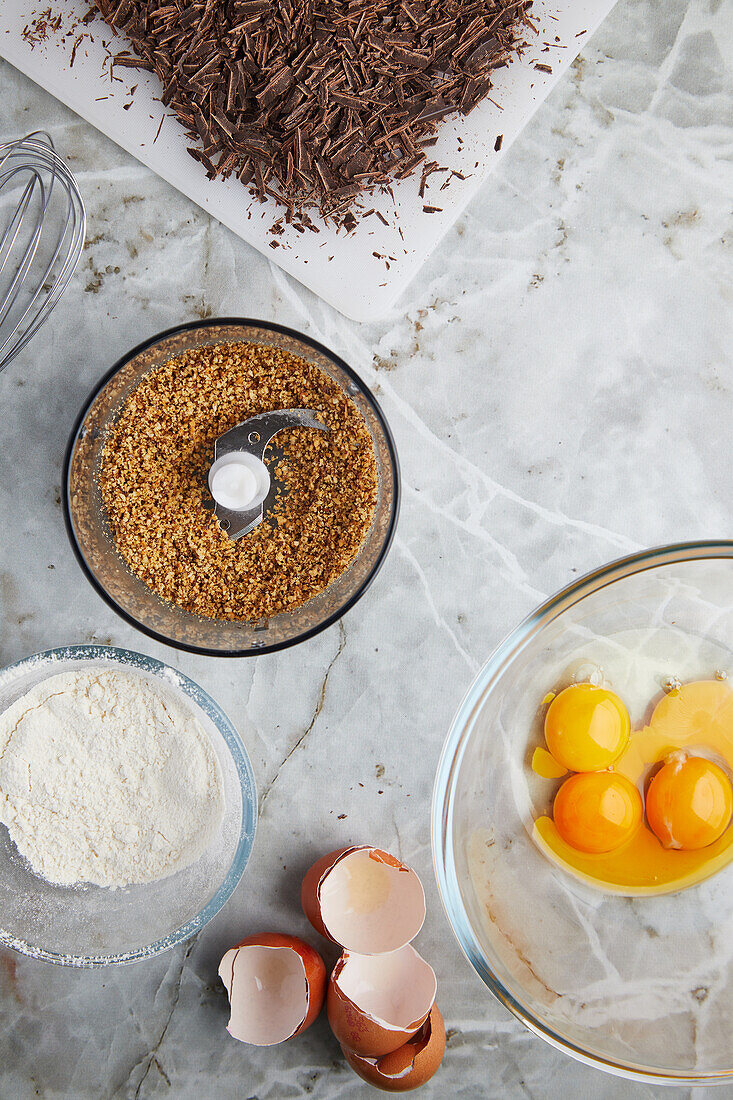 Top view of egg yolks in glass bowl placed on marble table near crushed cookies flour and chocolate shavings for pastry cooking