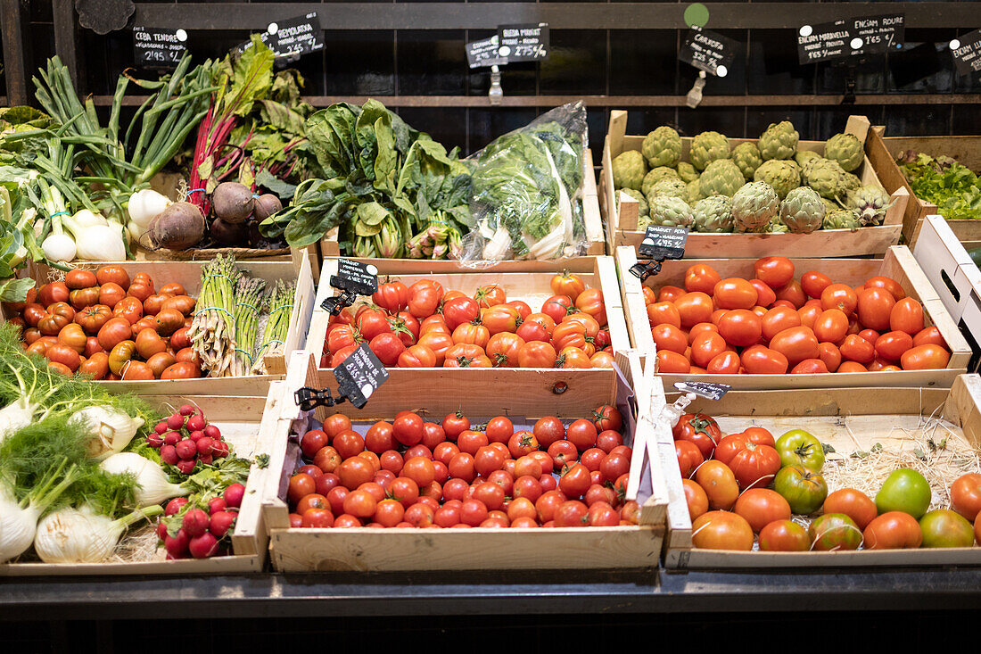 Verschiedene frische, reife Bio-Tomaten und Gemüse in offenen Pappschachteln mit Preisschildern für jedes Produkt in einem Einzelhandelsgeschäft