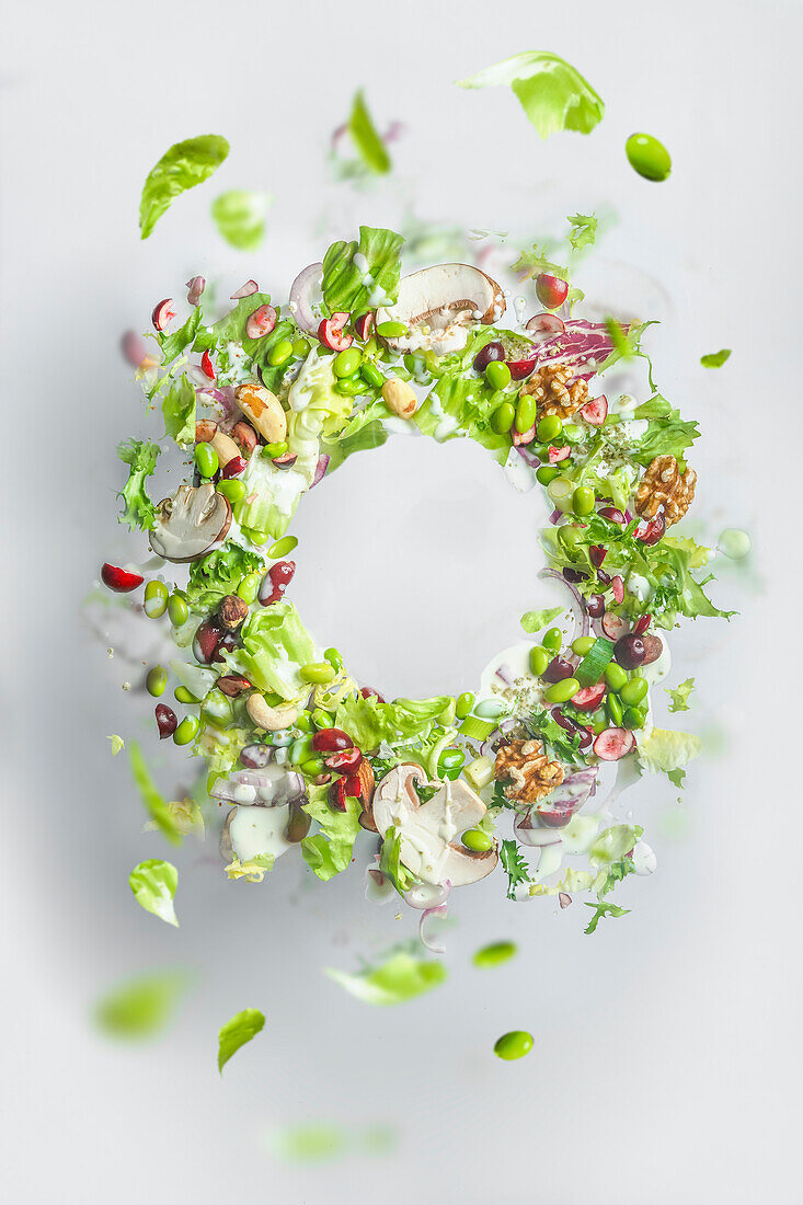 Kreisrahmen eines fliegenden gesunden grünen Salats mit Salat, Nüssen, Bohnen, Dressing und Gemüse. Ausgewogenes veganes Essen mit Kopierraum. Schweben von Lebensmitteln