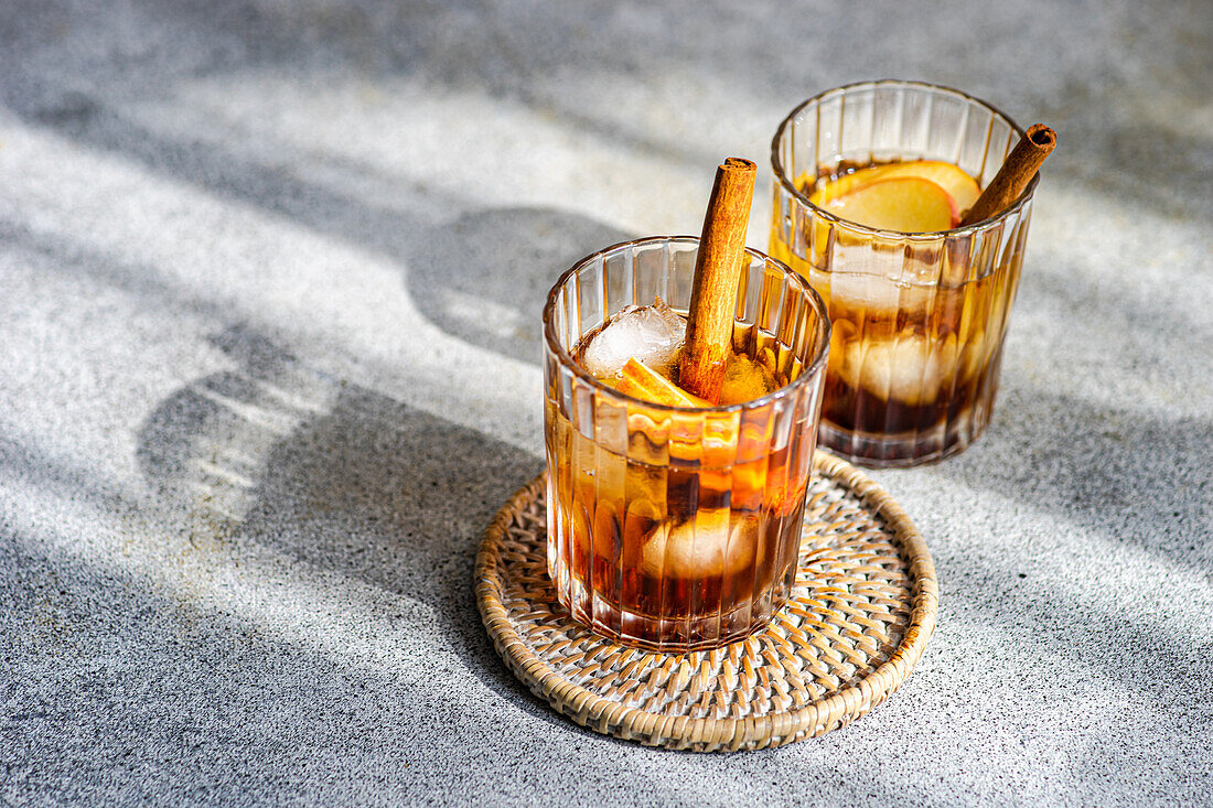 From above of fresh apple cider cocktails garnished with cinnamon sticks star anise and apple slices in a crystal glass filled with ice cubes on a textured background