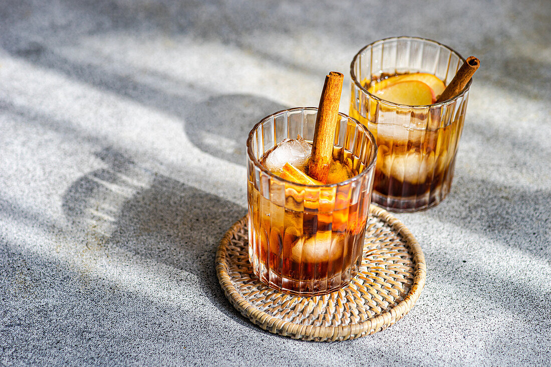 Von oben auf frischen Apfelwein-Cocktails garniert mit Zimtstangen, Sternanis und Apfelscheiben in einem mit Eiswürfeln gefüllten Kristallglas auf einem strukturierten Hintergrund
