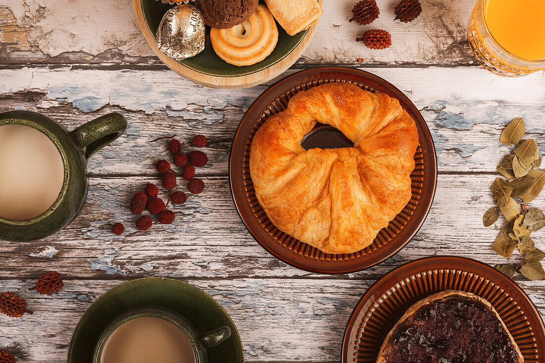 A rustic breakfast table with a fresh pastry, cups of coffee, and glasses of orange juice.