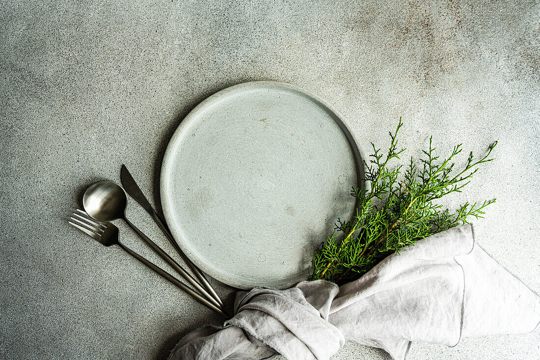 From above of Christmas composition of plate and fork and knife next to a bunch of green fir trees wrapped in a cloth placed on gray background