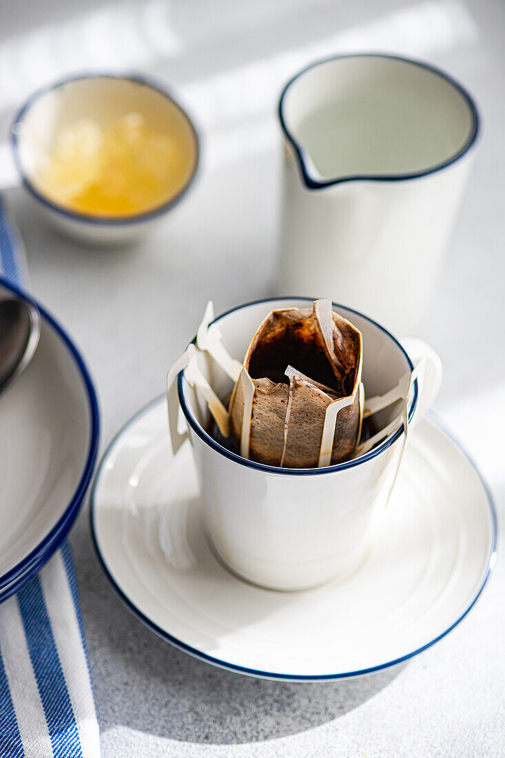 A serene scene of a drip coffee cup with a filter, placed on a plate alongside a silver pitcher and a bowl of honey, bathed in soft morning light.