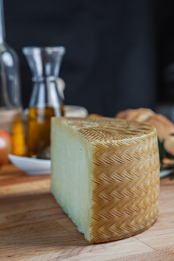 A fresh block of artisanal cheese presented on a wooden table, accompanied by olive oil and rustic kitchen background.