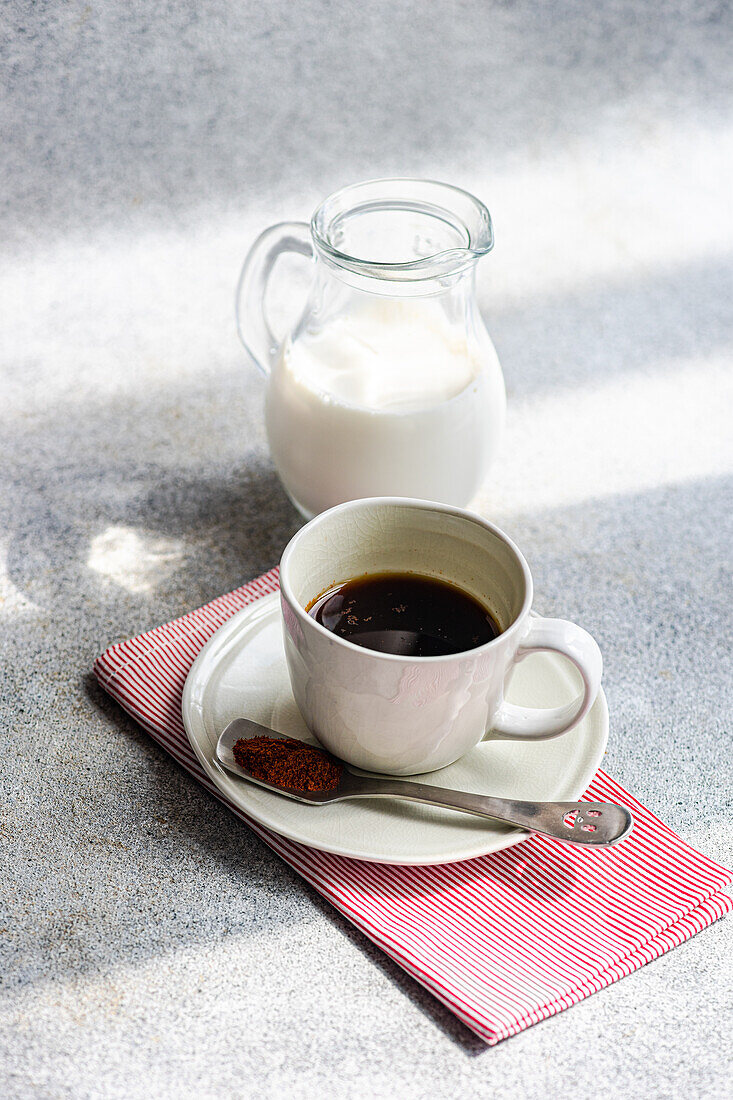 Hochformatige Tasse würziger Espresso neben Löffel mit roter Paprika auf grauem Tisch neben Milchflasche im Tageslicht