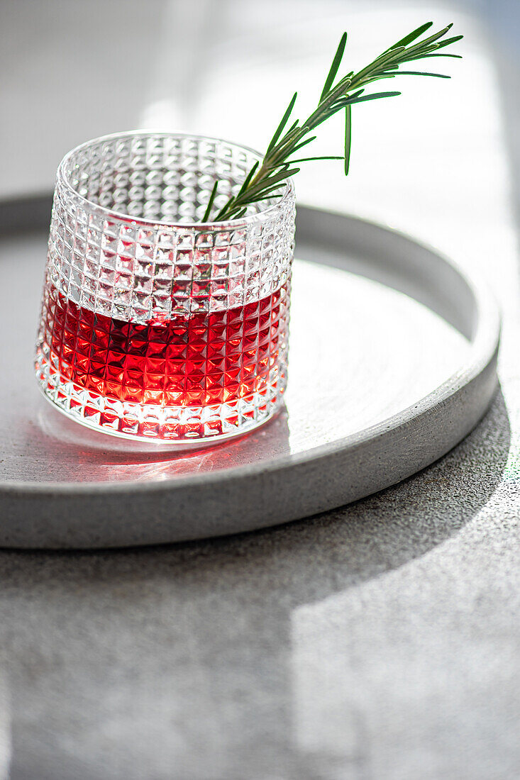 Elegant cocktail with cherry and apple juice mixed with vodka garnished with a fresh rosemary sprig presented on a circular tray