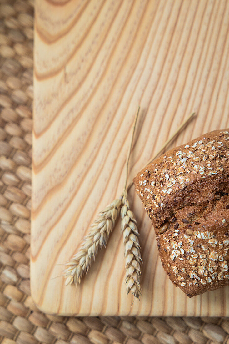 A loaf of seeded bread beside a wheat ear, placed on a wooden board over a woven mat, showcasing natural ingredients