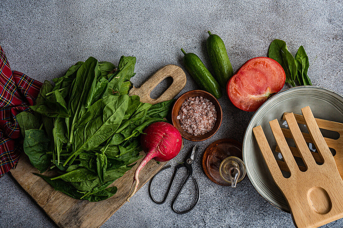 Top view of array of fresh ingredients including spinach, tomatoes, zucchini and spices on textured surface, complemented with wooden utensils and a rustic pair of scissors