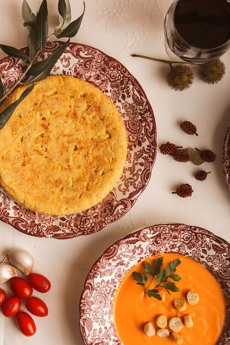Draufsicht auf elegante spanische Omelette- und Salmorejo-Gerichte mit einem Glas Wein auf einem weißen Tisch