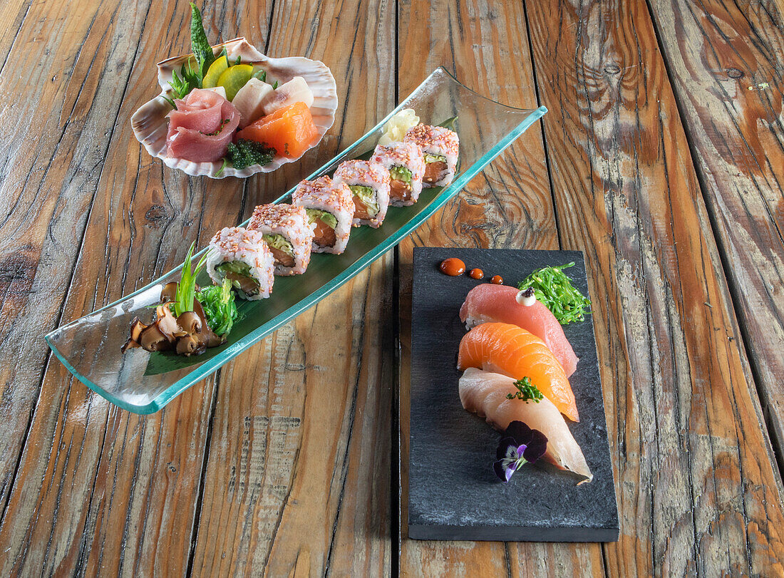 From above of delicious uramaki sushi and nigiri sushi together with sashimi in small bowls on wooden background