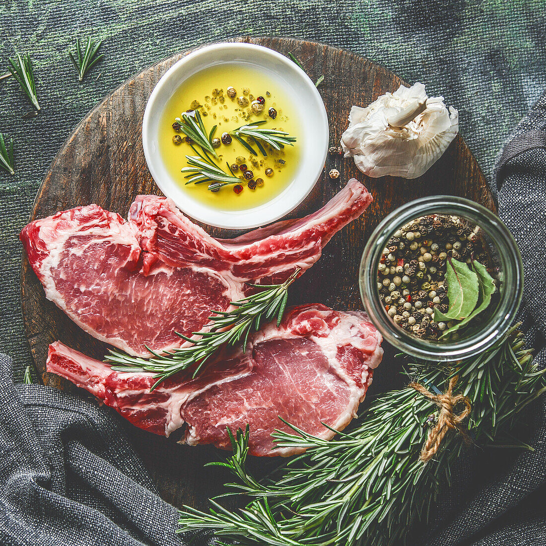 Raw meat chop on wooden cutting board with rosemary, herbs, spices and cooking oil. Top view
