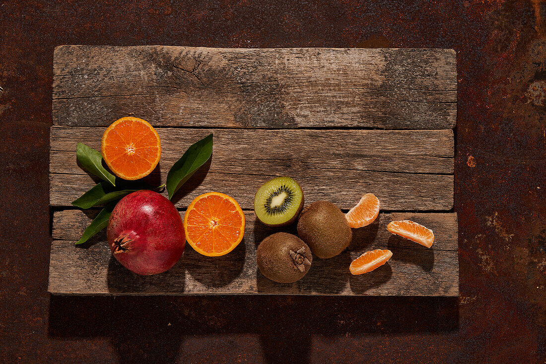 Frische reife Kiwi- und Orangenscheiben neben einem Granatapfel auf einem Holzbrett von oben gesehen