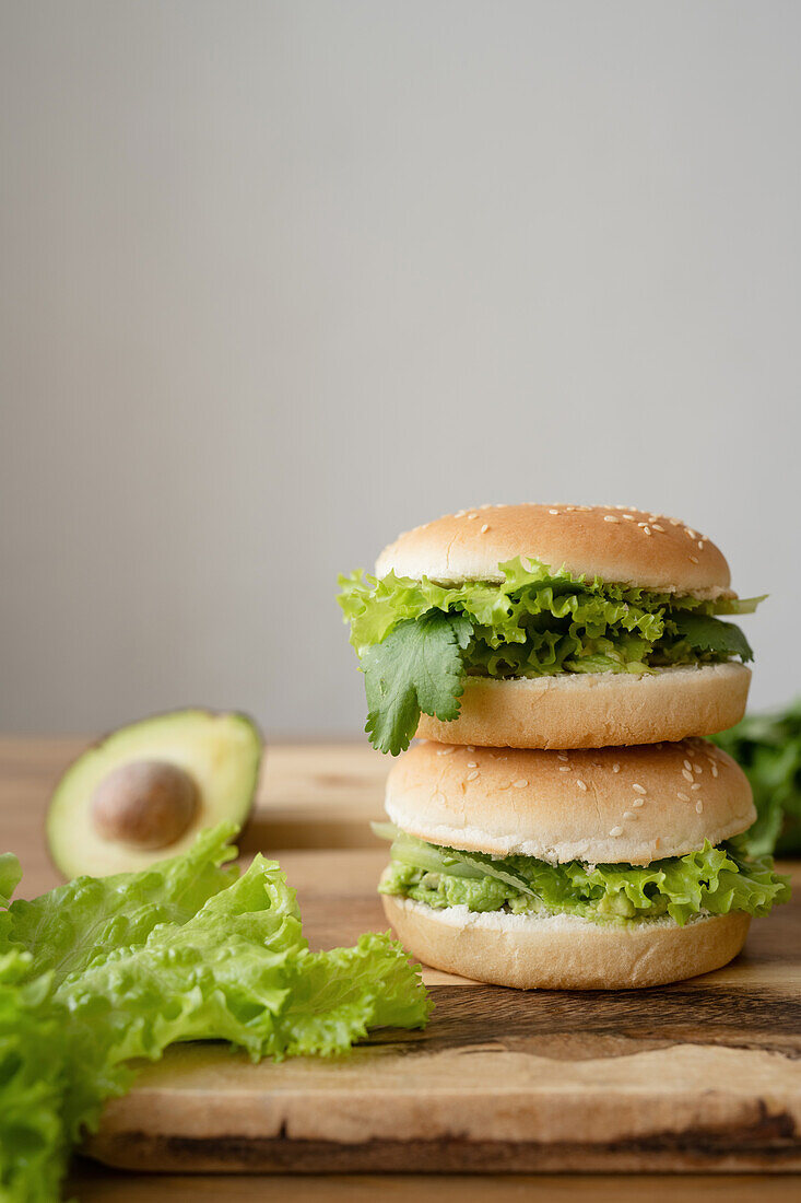 Tasty vegetarian burger with fresh lettuce and sliced avocado on wooden cutting board against gray background