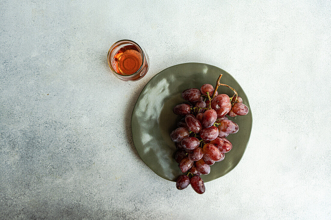 Top view of red Champagne grape variety served on dark plate near pink champagne wine in glass against gray background