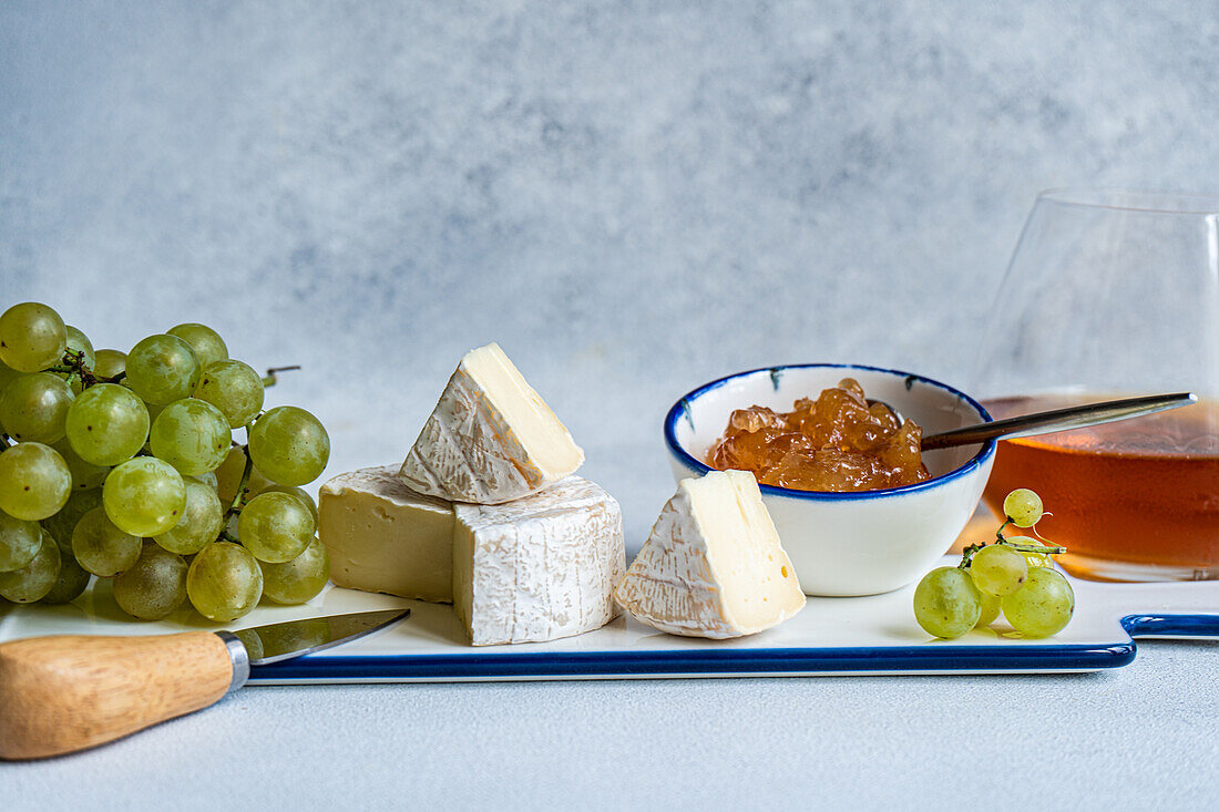 Assorted yummy snacks with different types of cheese and sweet served on ceramics plate with grapes