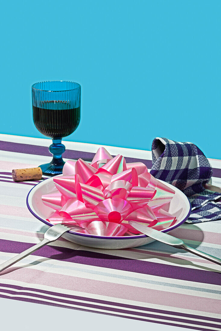 Generatives KI-Bild eines skurrilen Valentinstags-Setups auf einer gestreiften Tischdecke mit einem Glas, einem Teller mit einer riesigen rosa Schleife und einer Serviette
