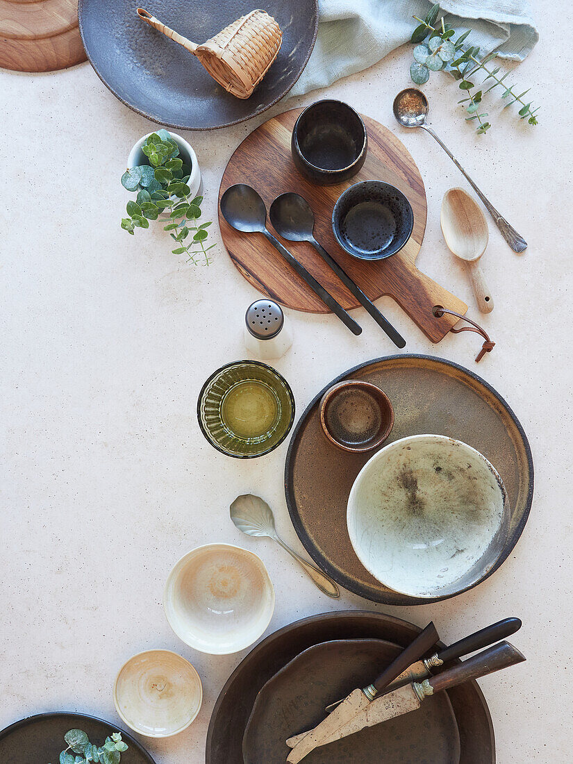 Top view of ceramic bowls with various different clean empty dinnerware and green herbs placed on white marble surface in modern restaurant