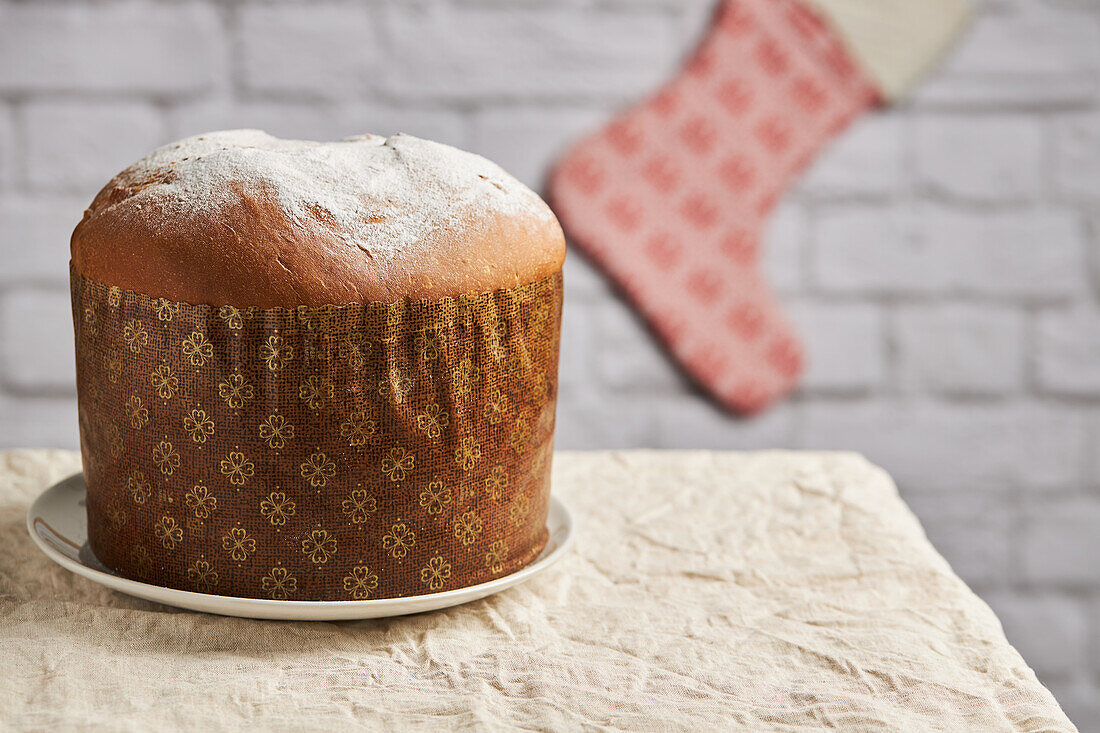 A panettone, showcased on a table, is complemented by a dangling Christmas stocking in the backdrop