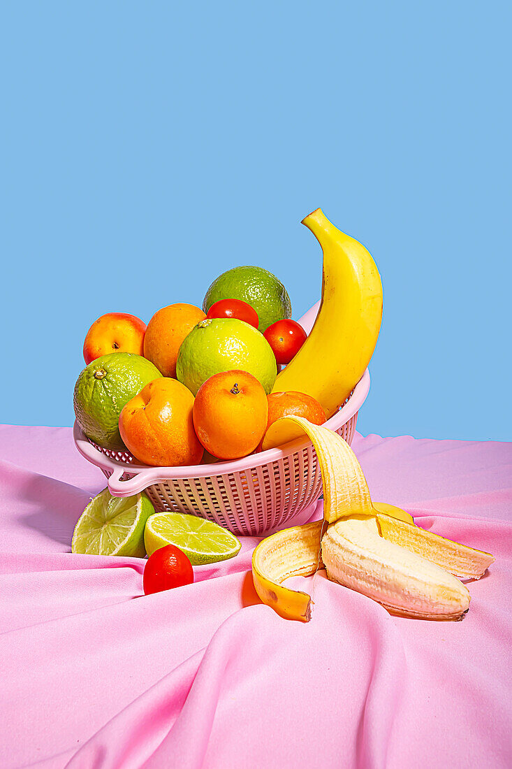 Plastic bowl with fresh assorted fruits placed on at table with a pink tablecloth table in daylight on blue background