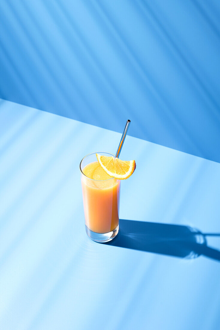 Draufsicht auf gepressten Orangensaft garniert mit Orangenscheibe auf blauem Hintergrund
