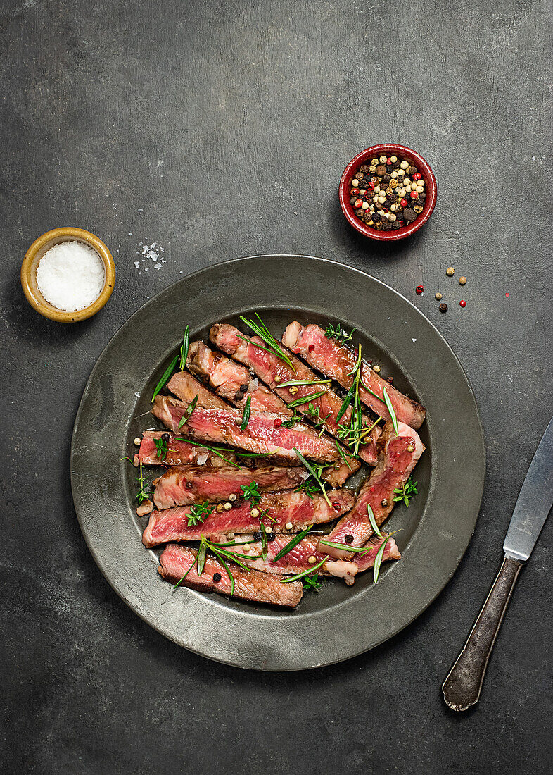 From above delicious sliced roast beef tagliatta served on plate near bowl with herbs placed on concrete table background