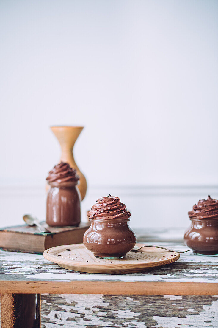 Delicious sweet chocolate mousse desserts in glass jars with silverware on wooden table against white background