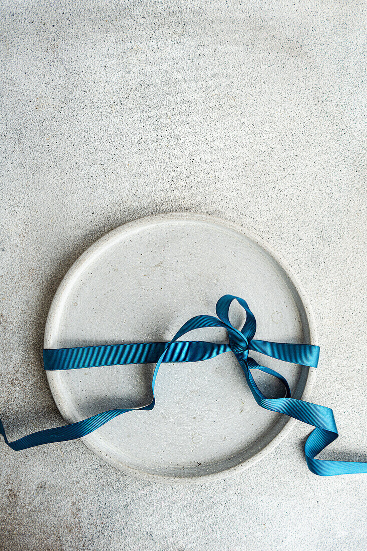 Top view of minimalist yet stylish Easter table setting, with a concrete grey plate bound by a rich blue ribbon, placed on gray surface