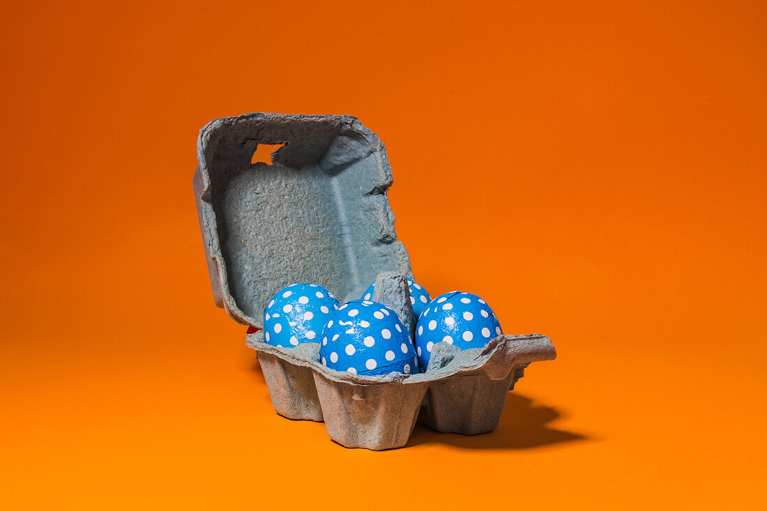 Nahaufnahme einiger blauer Ostereier in einer grauen Pappschachtel auf einem orangefarbenen Hintergrund