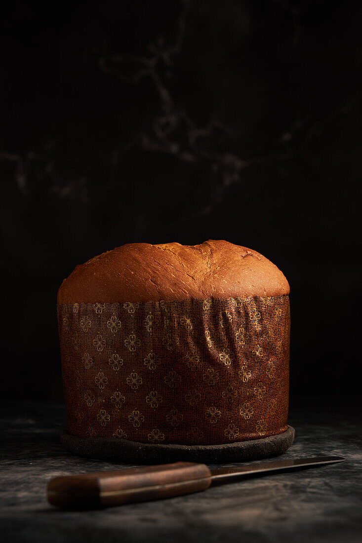 A sumptuous panettone sits in the shadows, adorned with an intricate lacy wrapper, exuding festive warmth and tradition