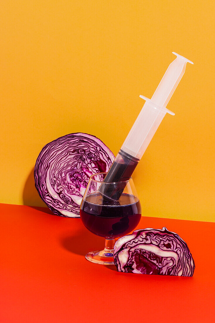 Antioxidant healthy juice of red cabbage vegetable extracted in glass with syringe on bright backdrop with cabbage