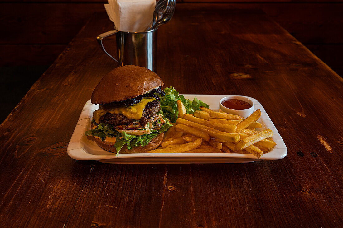 Hausgemachter Cheeseburger mit Käse und Gemüse, serviert mit Pommes frites und Salat