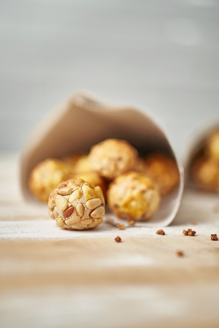 Sweet panellets in newsprint cones placed on wooden table against blurred white wall