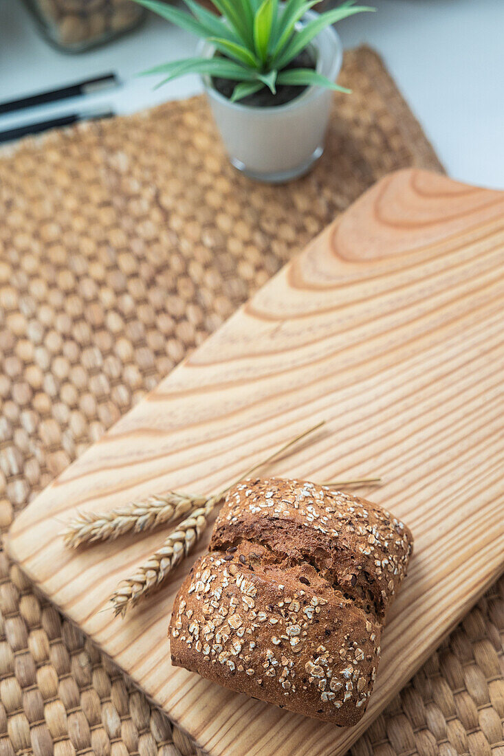 Ein Laib Saatenbrot neben einer Weizenähre, auf einem Holzbrett über einer gewebten Matte, mit natürlichen Zutaten