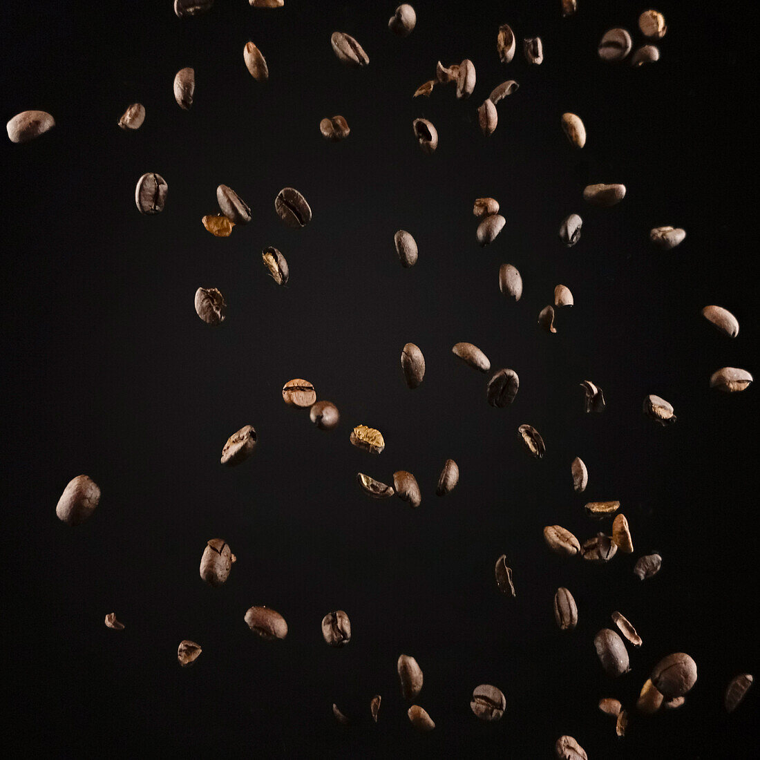 Fragrant roasted coffee beans falling against dark backdrop as concept of ingredient for tasty hot drink