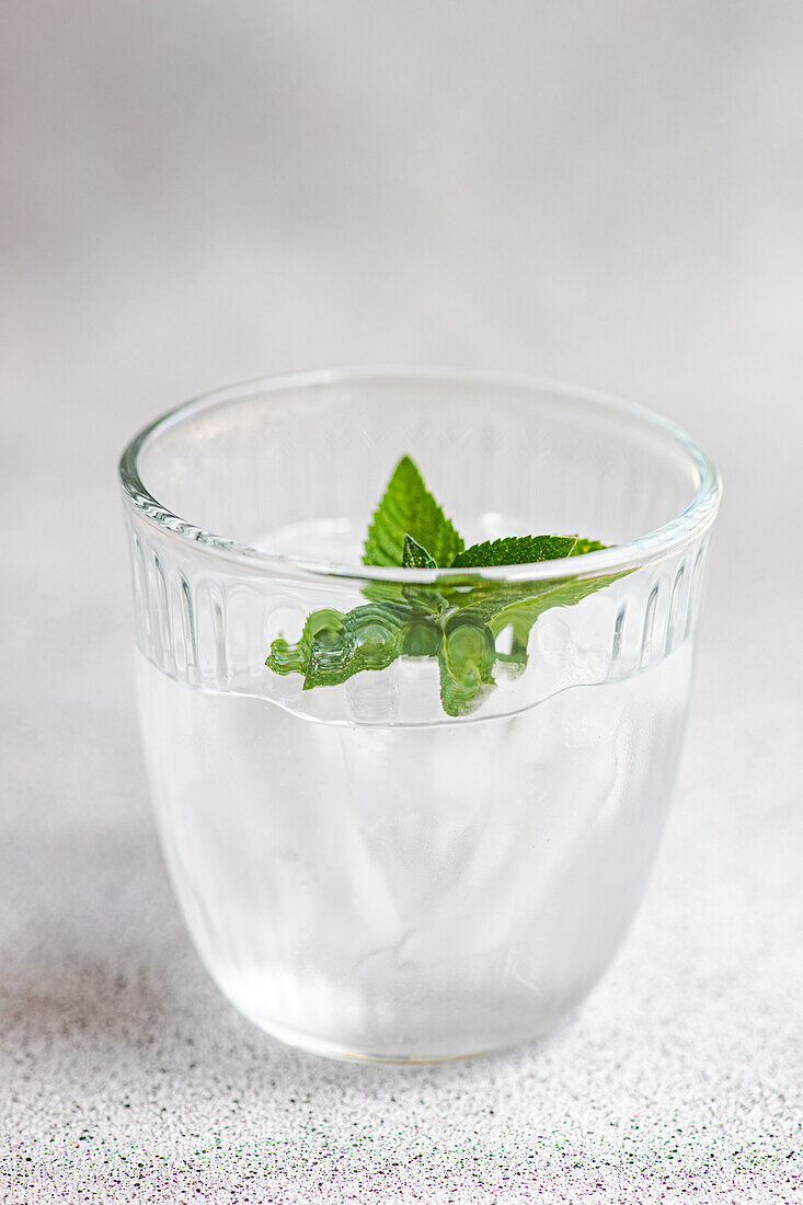 Glas Mineralwasser mit Eiswürfeln und frischen Minzblättern vor grauem Hintergrund