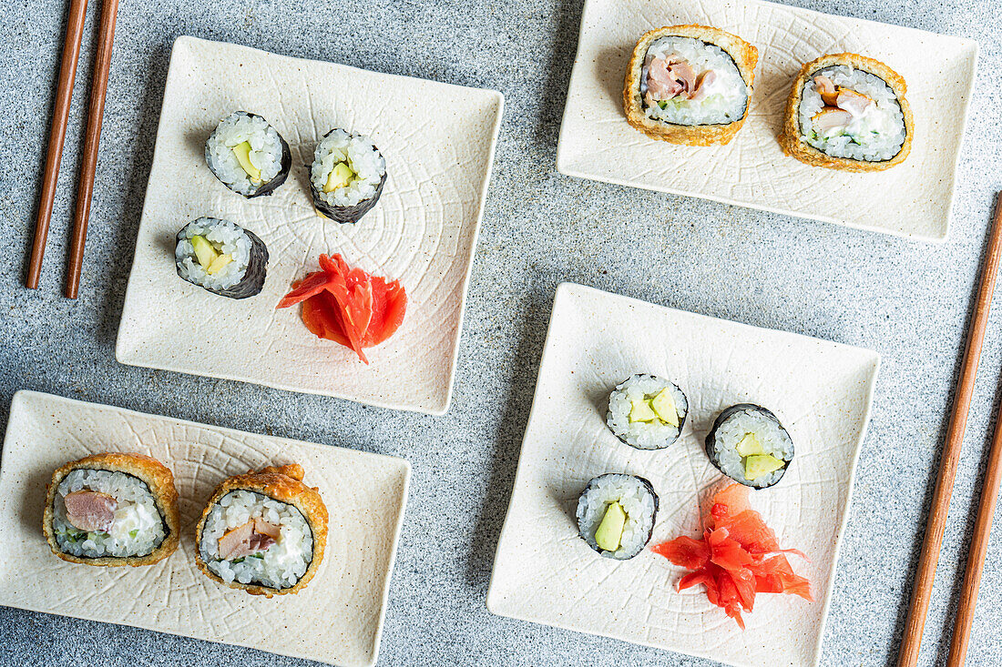 From above of various sushi rolls placed on plates with chopsticks and soy sauce on white background