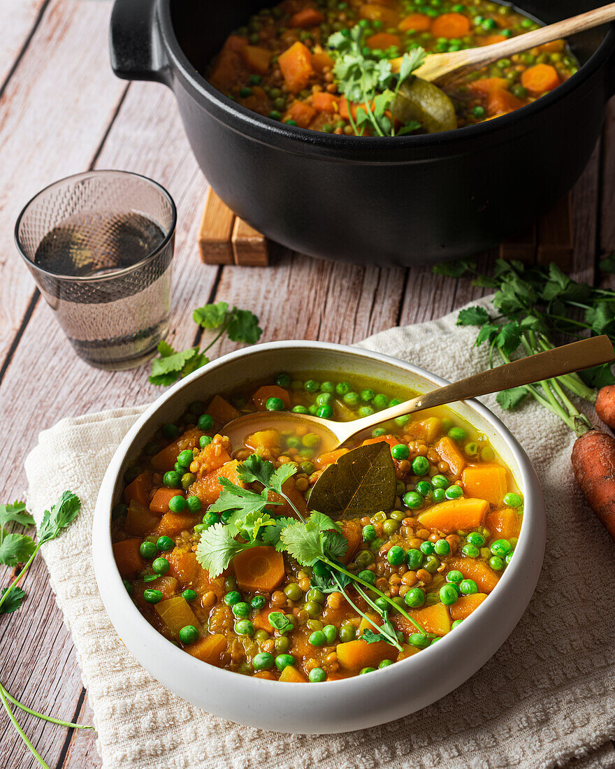 Top view of appetizing fresh cooked soup with carrot and green peas served in white ceramic bowl placed on wooden table and decorated with parsley branch