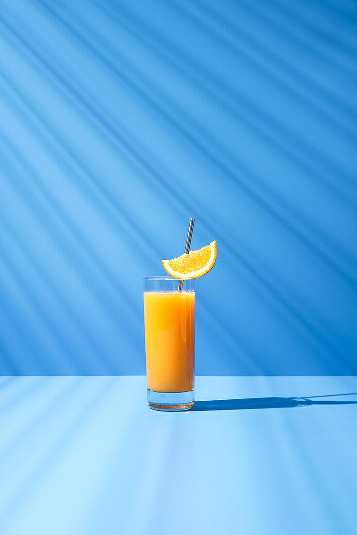 Squeezed orange juice garnished with orange slice on blue background
