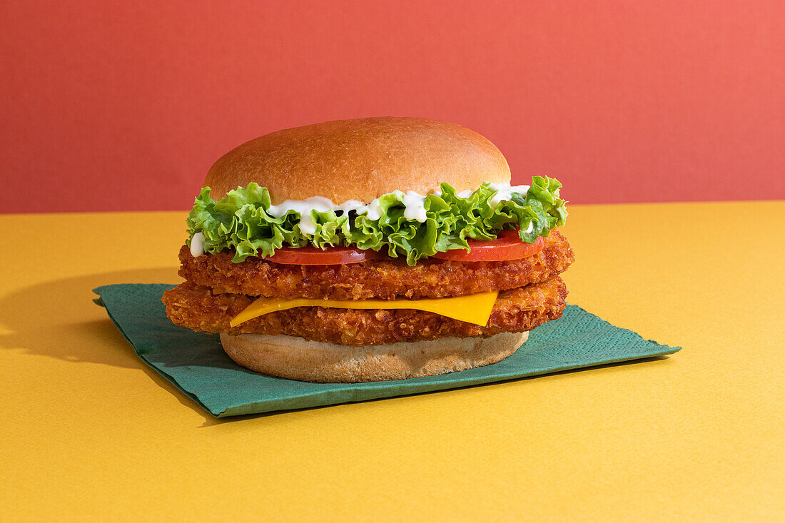 Delicious fish burger with tomatoes, cheese slices and fresh lettuce on yellow and red background