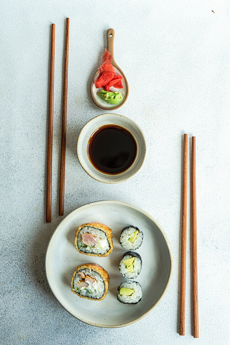From above of japanese food set with avocado maki roll and fried sushi with soy sauce and ginger placed on a white concrete table