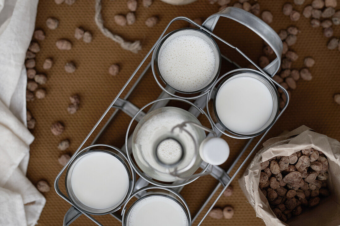 Draufsicht auf ein hausgemachtes Bio-Horchata-Getränk, serviert in durchsichtigen Gläsern und einer Flasche auf einem Holztisch neben Mandeln in einer rustikalen Küche