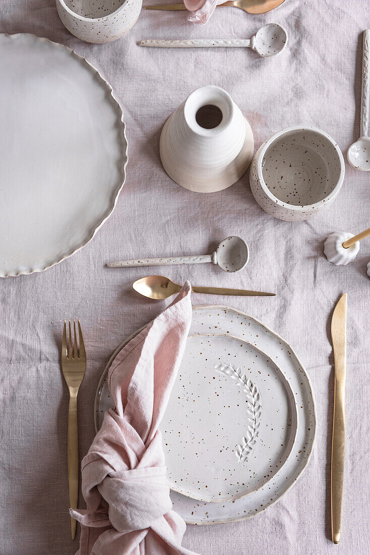 Draufsicht auf einen festlich gedeckten Tisch mit verschiedenem Geschirr und Besteck auf einer rosa Serviette