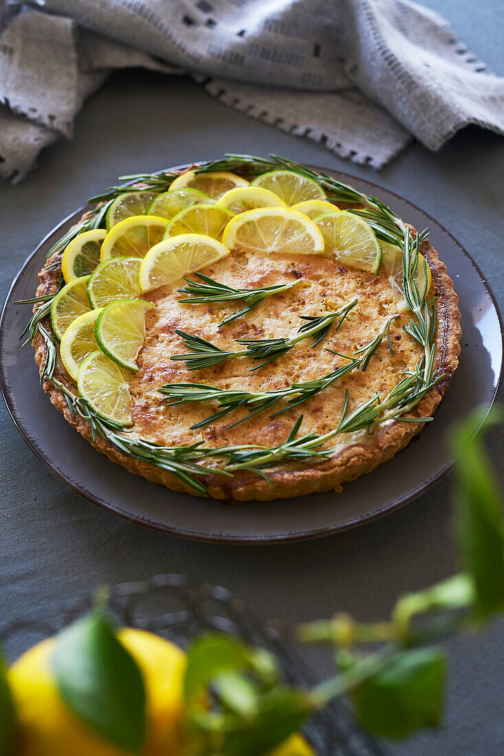 From above of round lemon pie with decorated with lemon slices and rosemary sprigs on table in the kitchen