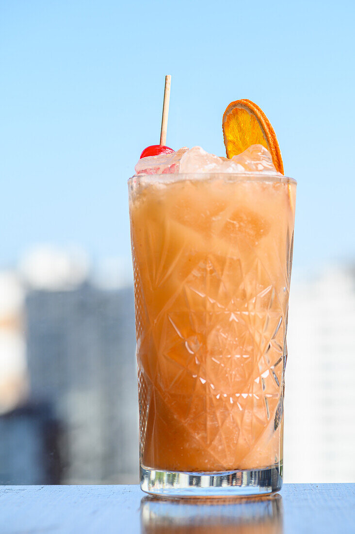 Glas kalten erfrischenden Sex on the Beach-Cocktail mit Eiswürfeln Kirsche und Orangenscheibe gegen verschwommene Stadt platziert
