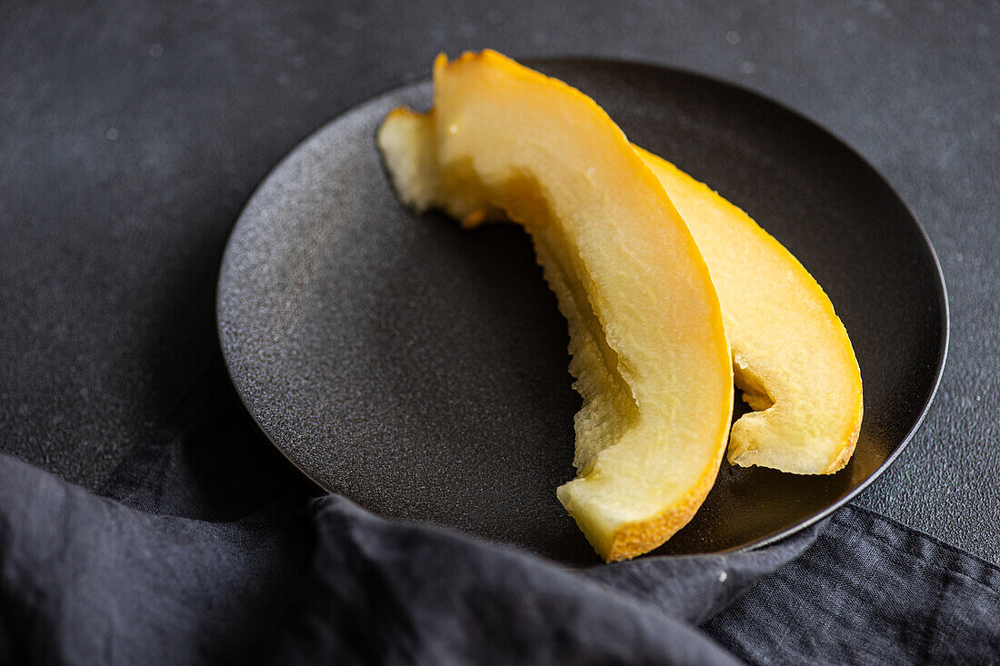 Top view of slices of sweet ripped melon served in ceramic plate on concrete black table
