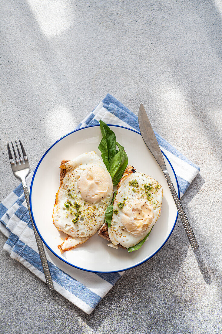 Top view of plate of healthy toast with fried egg pesto sauce and green herbs served on gray table during breakfast