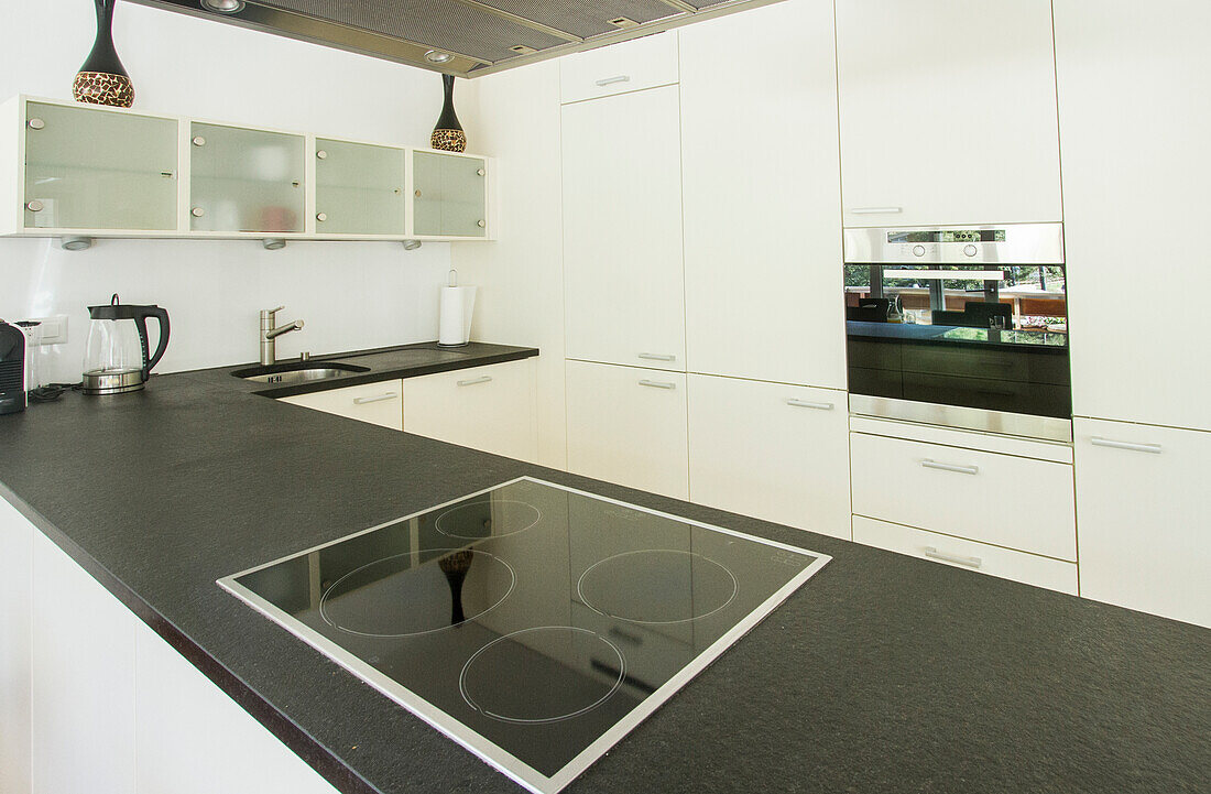 Eine gut organisierte weiße Küche mit einer dunklen Arbeitsplatte, einem Elektroherd, Hängelampen und geräumigen Schränken